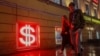 Young people walk past an illuminated US dollar sign